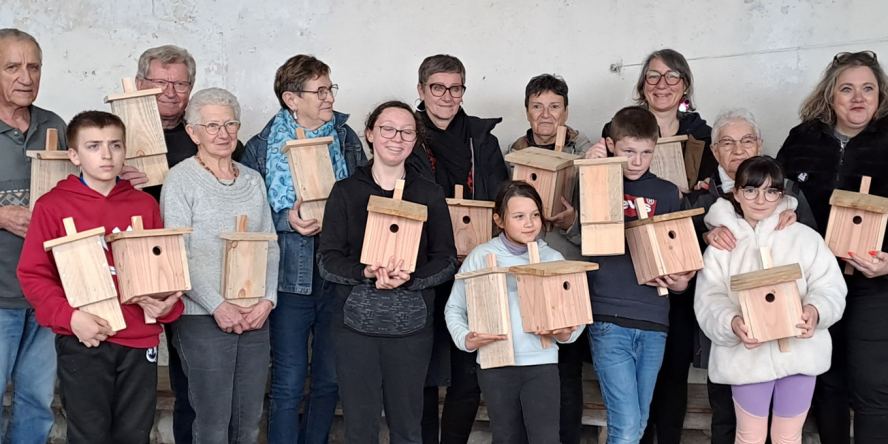 Un groupe d'enfants et d'adultes debout prenant la pose pour la photo avec des nichoirs en bois dans les mains.